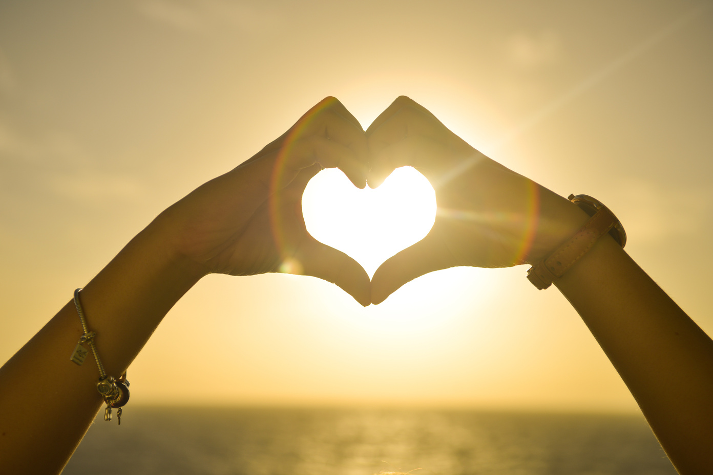 Two People Forming Heart Sign Against the Sun